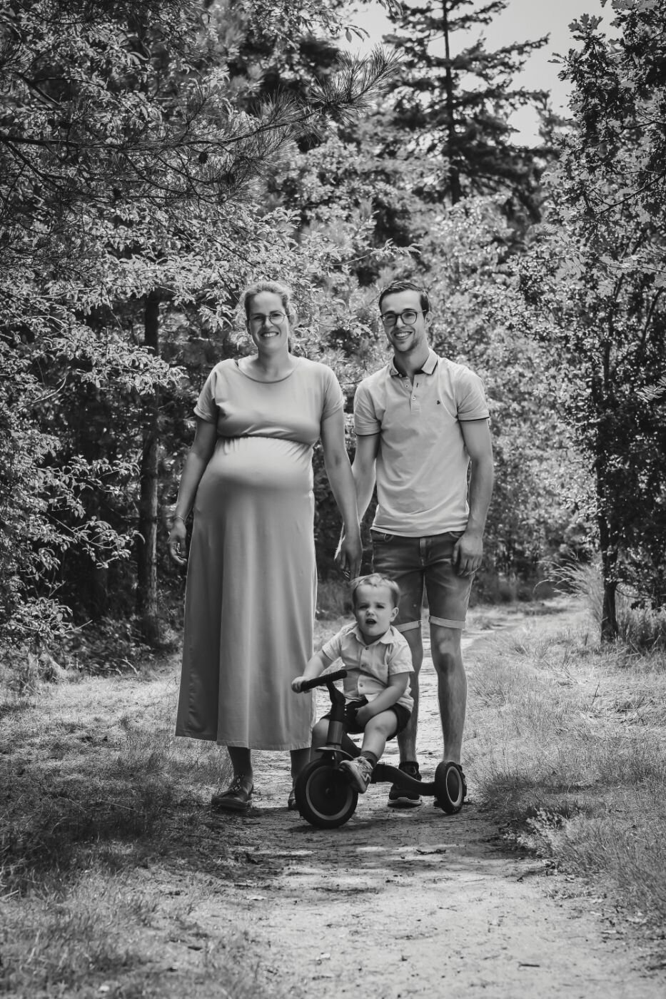 Zwart-wit foto van gezin met kind op driewieler in bos.