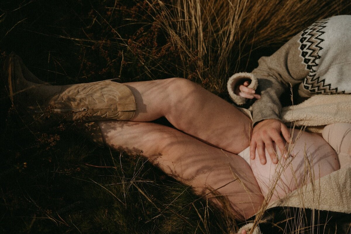 Détail de jambes croisée et ventre rebondi d'une jeune femme, ombres de brindilles sur la peau. Photographe Kamescop, reportage intime.