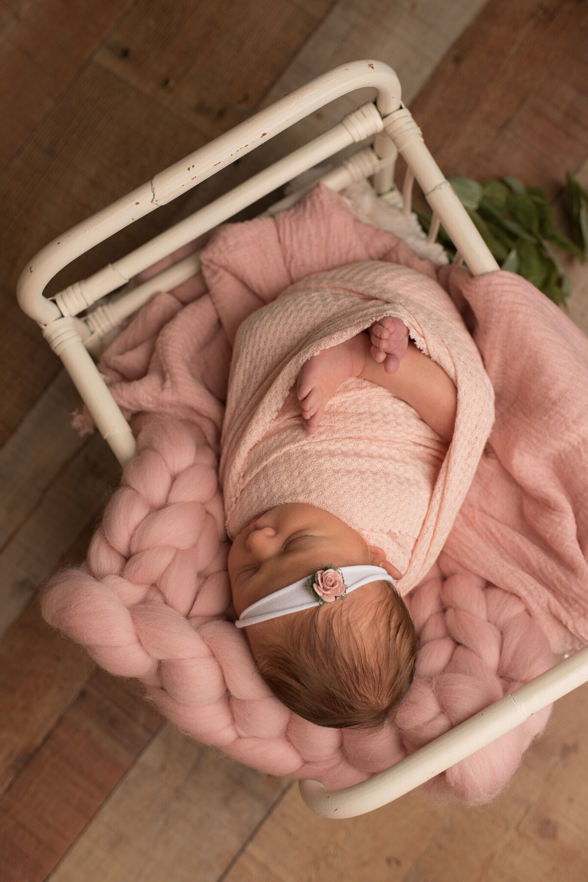 Baby girl lying in white crib, wrapped in pink with greens under her feet