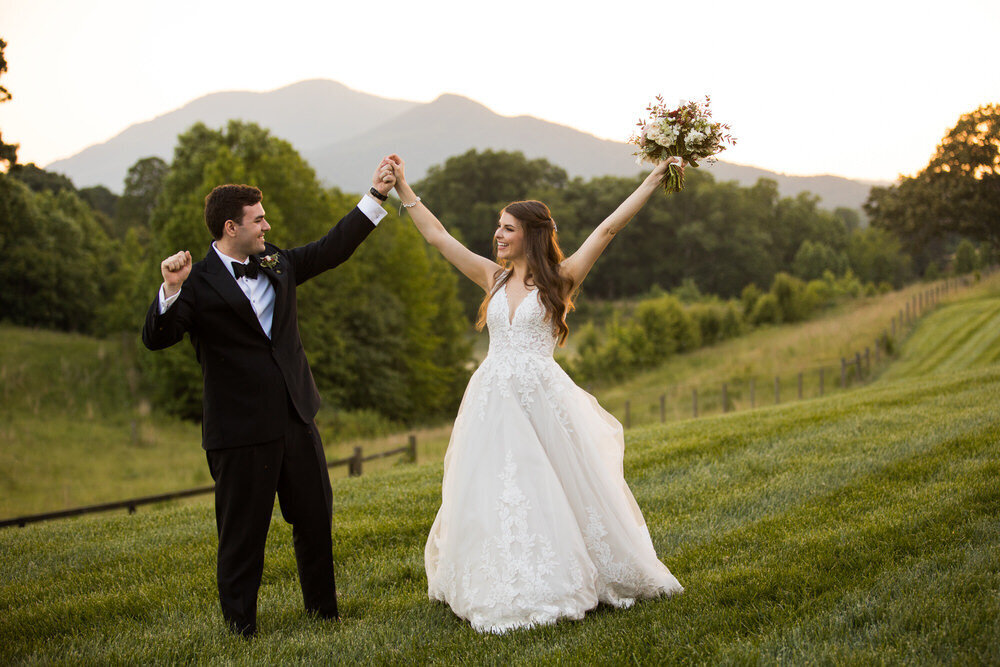 couple raises their arms in celebration against a beautiful mountain backdrop at a farm in nc