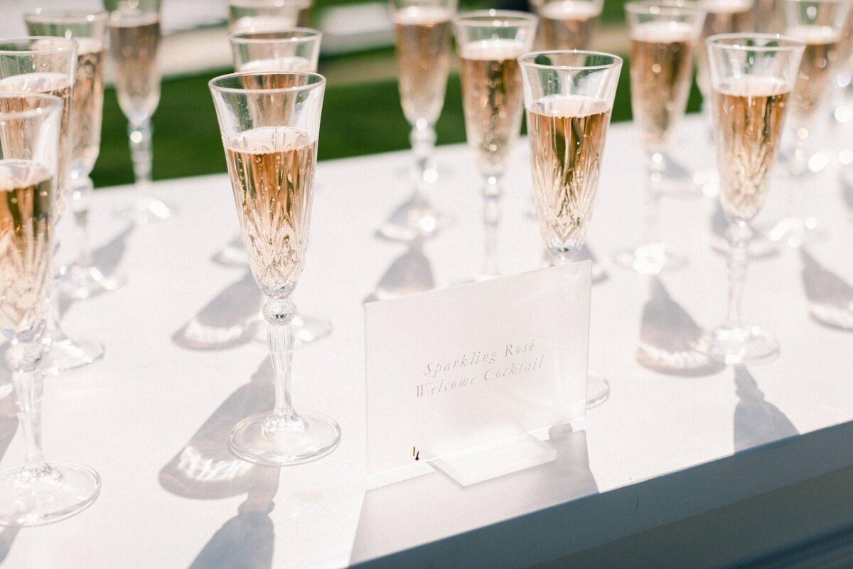 Rows of champagne glasses beside a "sparkling rosé" sign on a table.