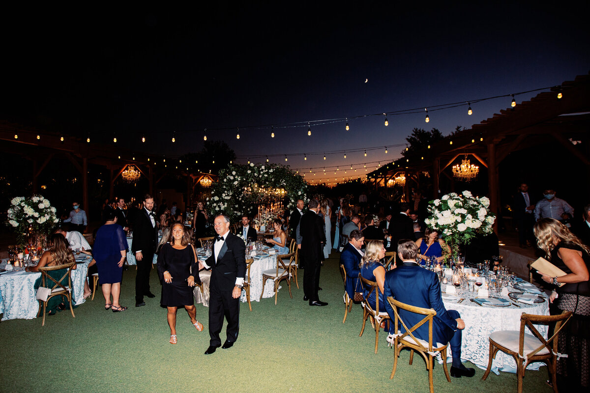 An enchanting outdoor wedding reception under twinkling string lights, featuring lush floral decor and elegantly dressed guests.