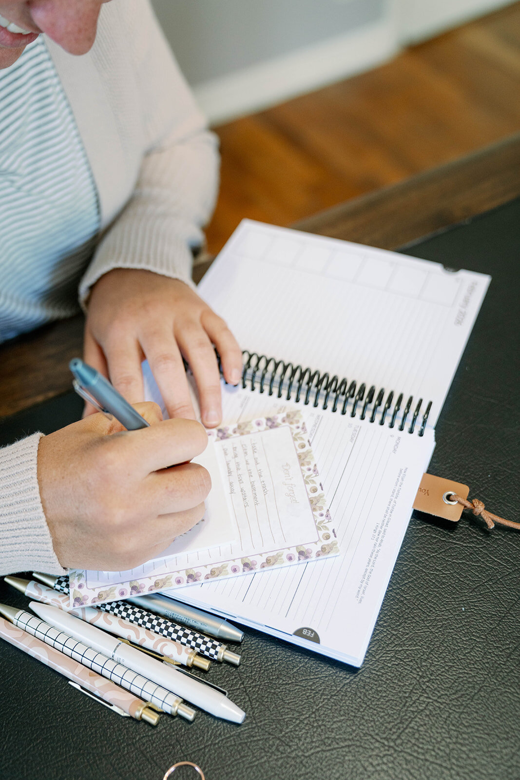Close-up of hands writing in a floral planner with pens and notebooks during the Indiana branding session.