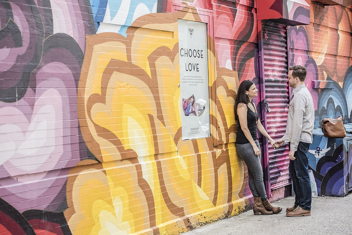 A couple holding hands while one leans on a mural