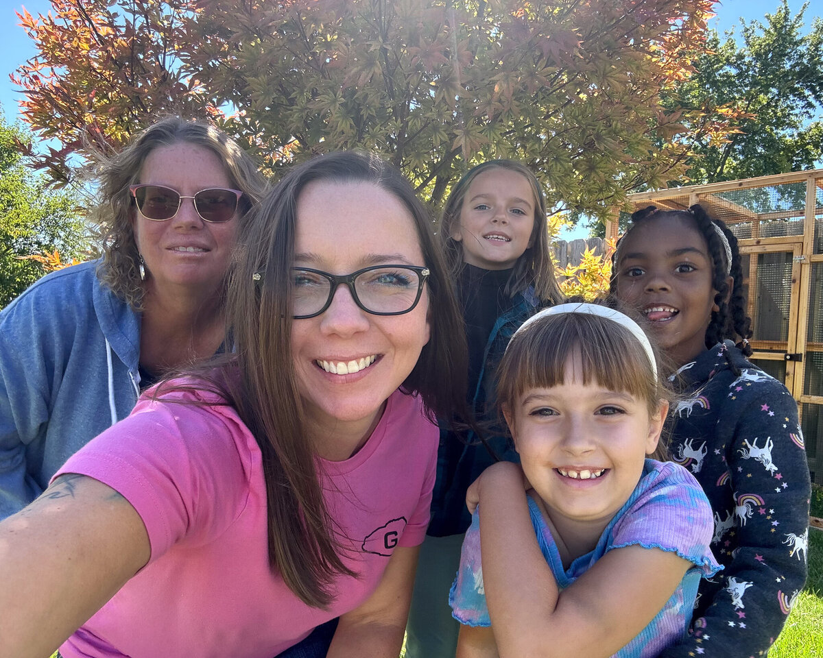 grandma, adult daughter, and 3 young nieces, standing in front of a tree, smiling at the camera