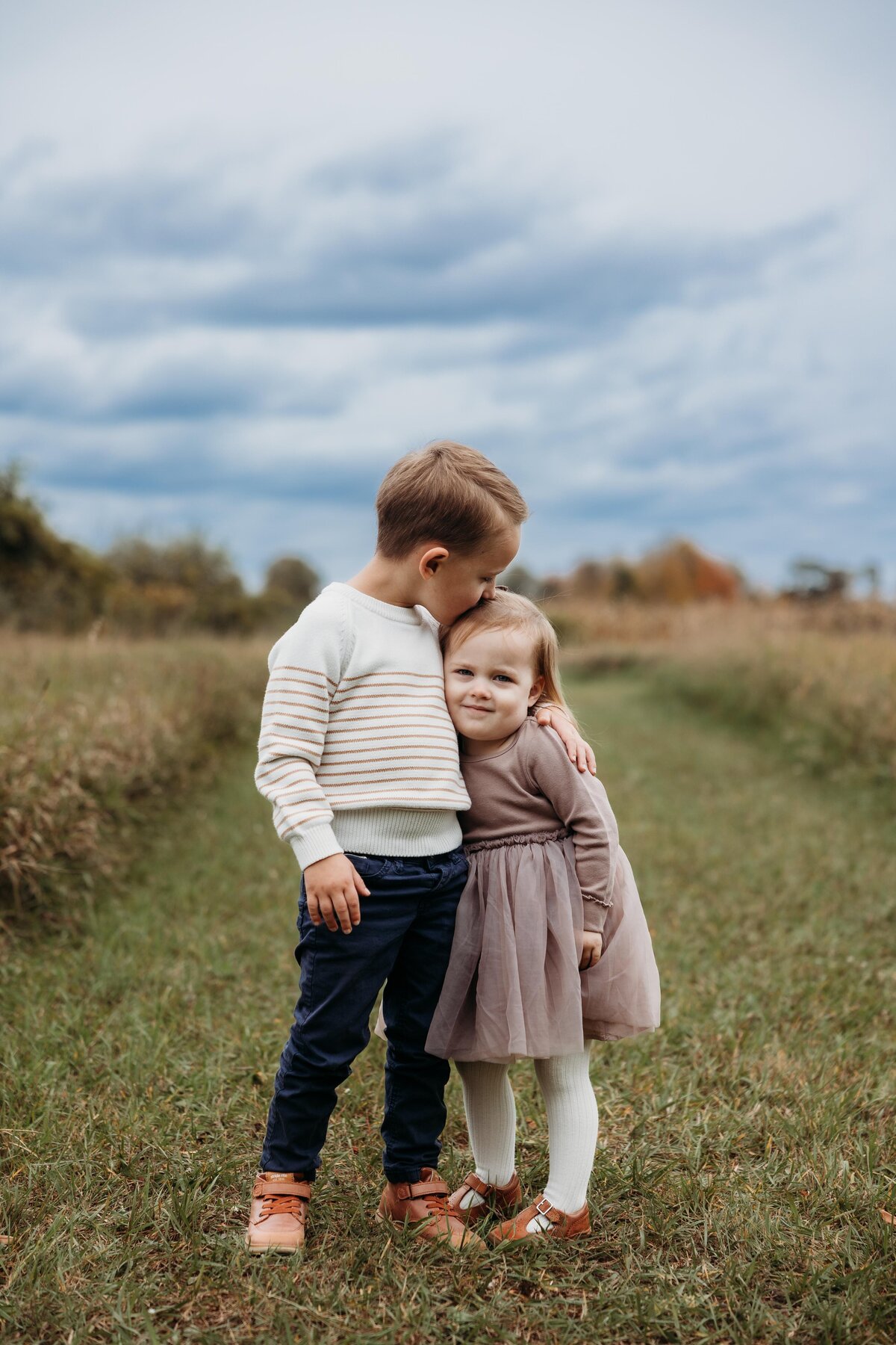 Big brother kissing sister on the head in a field.