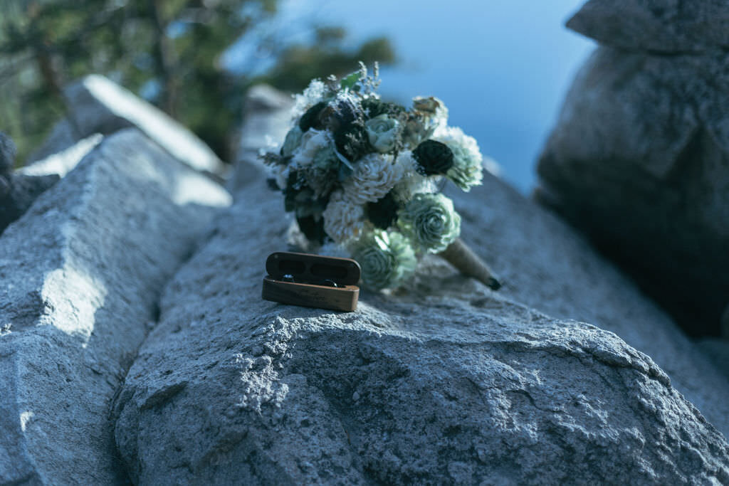 A bouquet of flowers and wedding rings sitting on a rock.