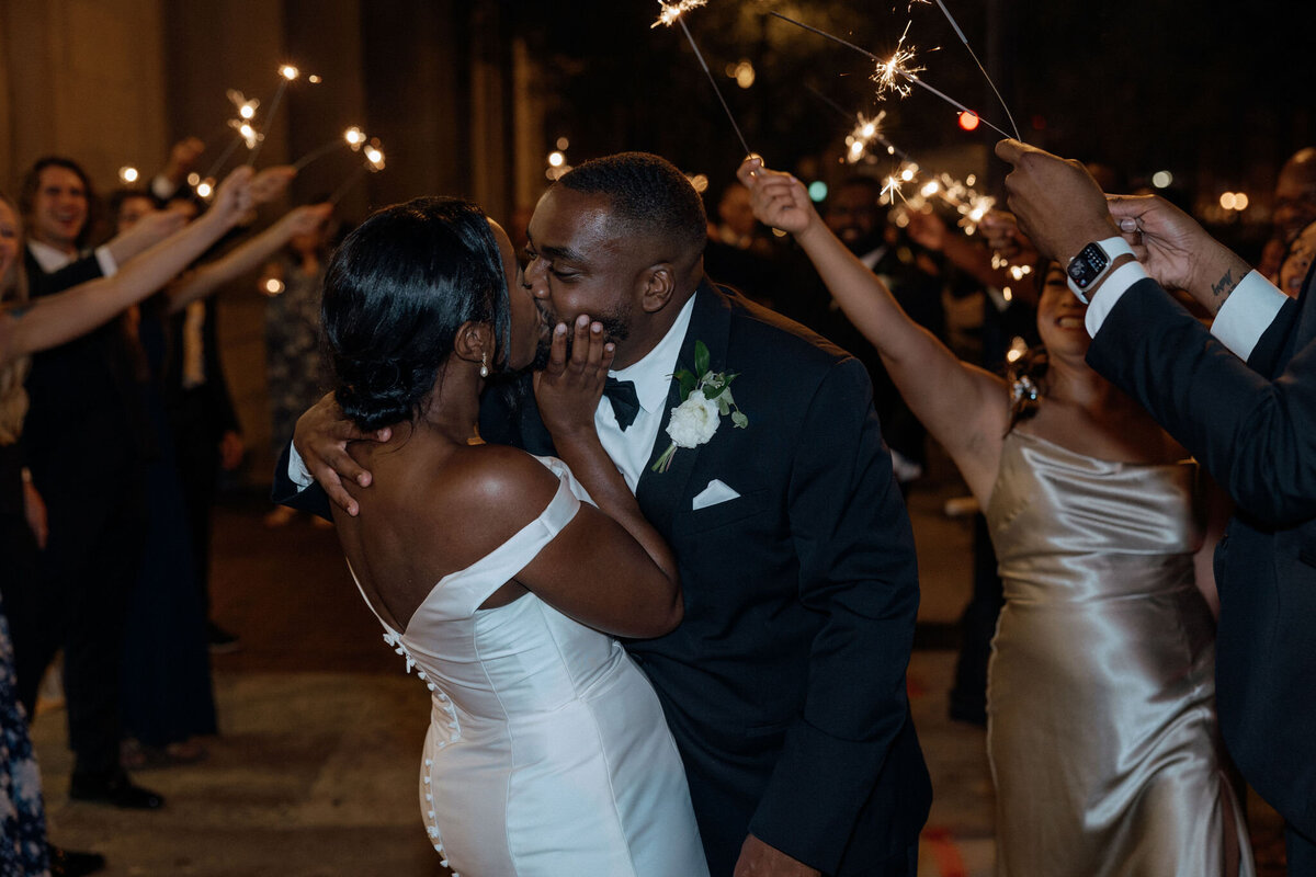 Bride and Groom exit their reception at 1208 Washington Place under a tunnel of sparklers held by their guests.  The bride and groom share a kiss at the end of the tunnel.