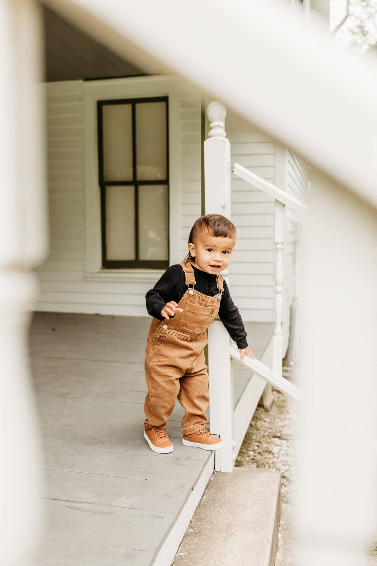 looking through the staircase as he walks down the steps, wearing corduroy overalls and black shirt.