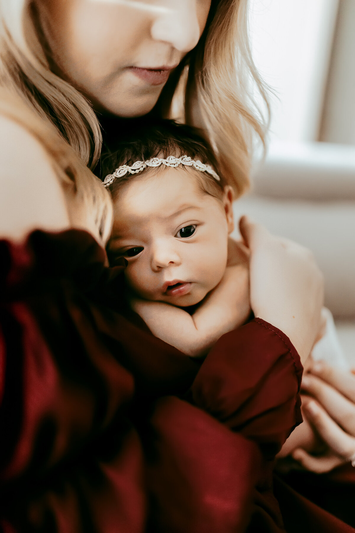 A woman in a maroon top holds a baby with a headband, nestled against her chest.