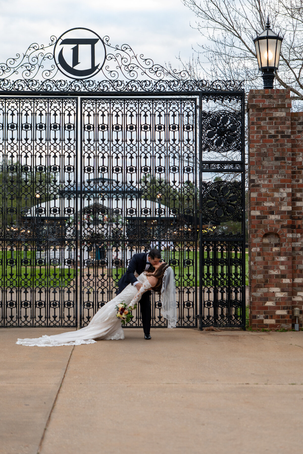 A person dipping their partner and kissing them in front of a grand gate on their wedding day 