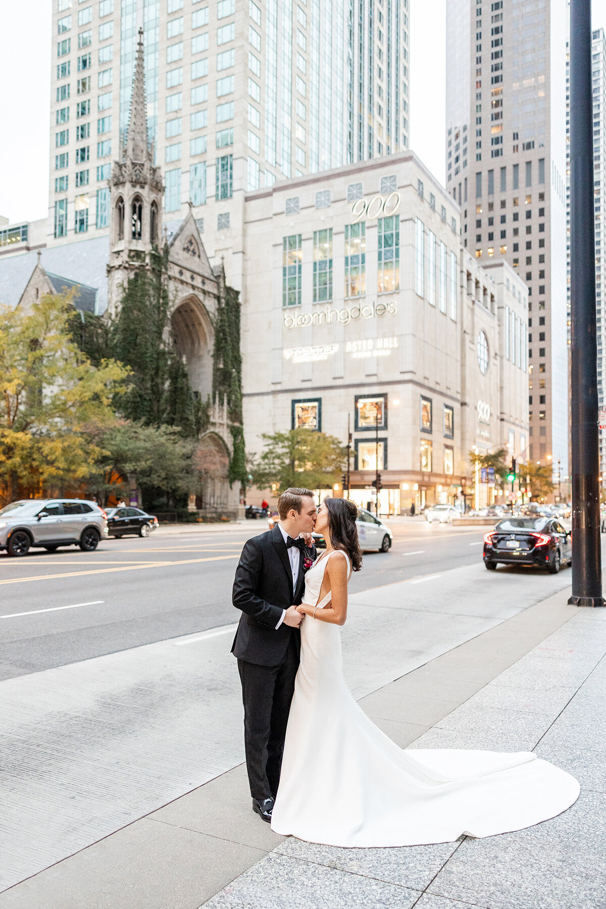 Bride and groom kissing on a city sidewalk with a church and buildings in the background