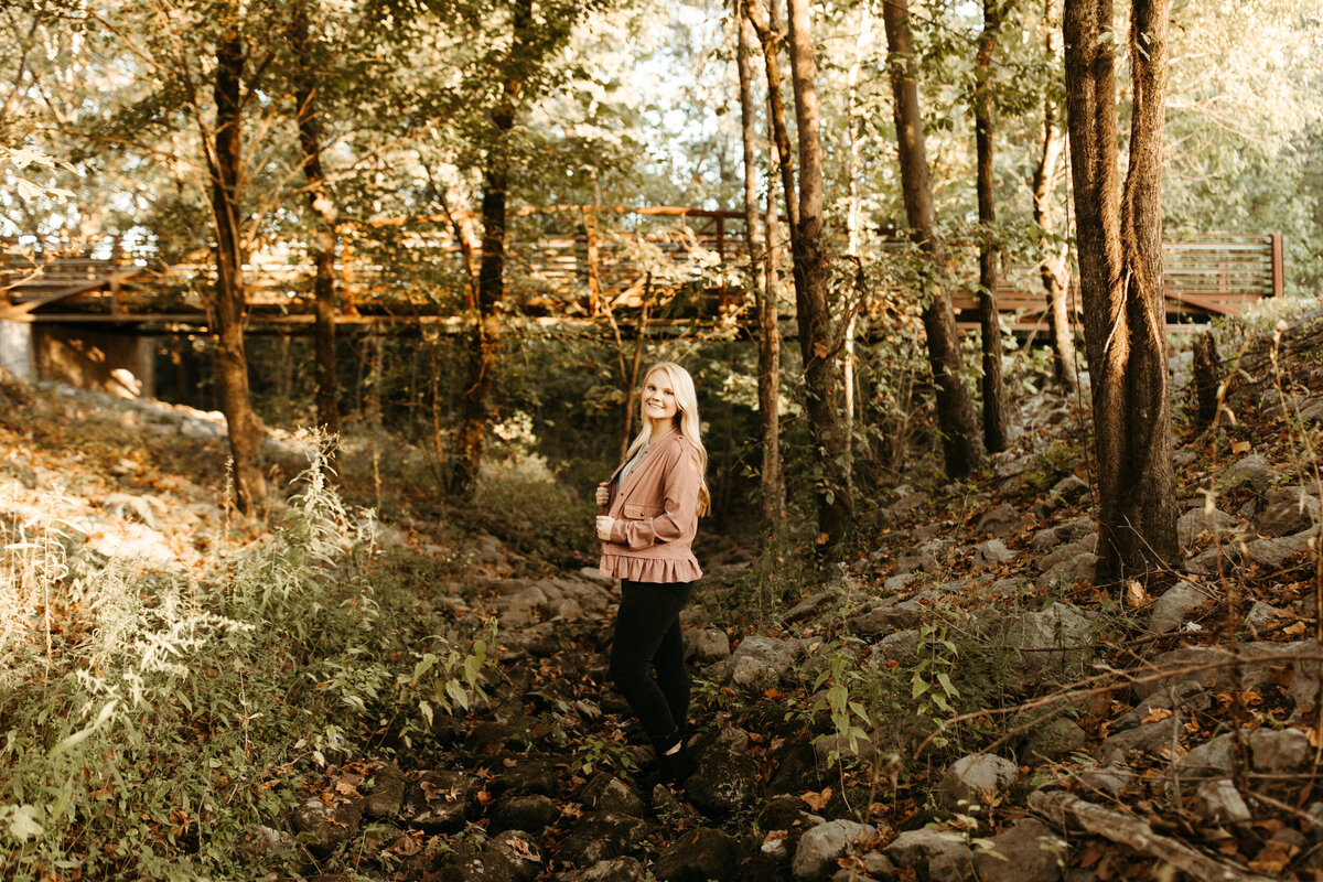 Wide angle view of girl senior posing in the woods underneath bridge