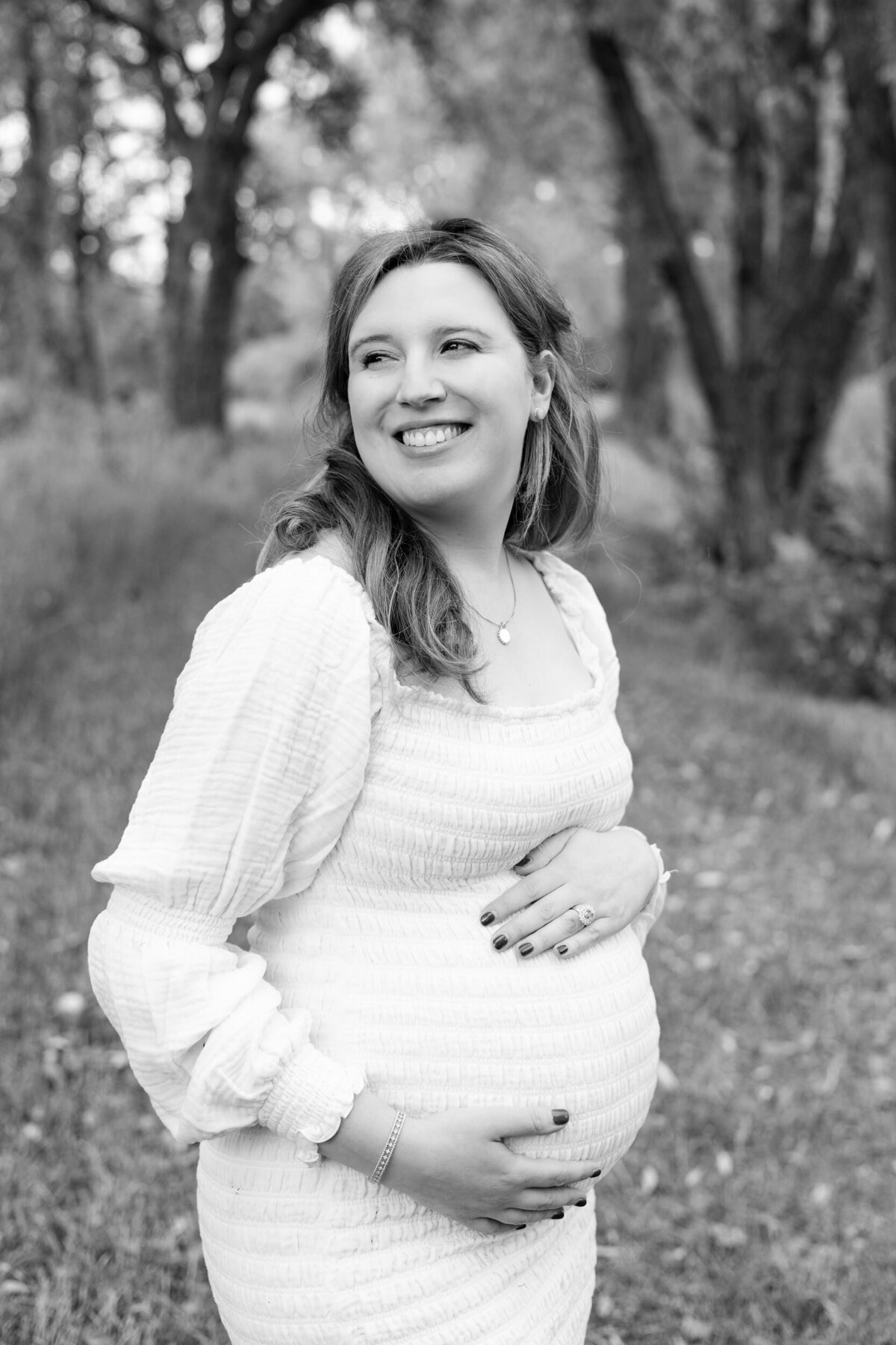 Black and white image of a pregnant woman holding her bump and smiling over her shoulder.