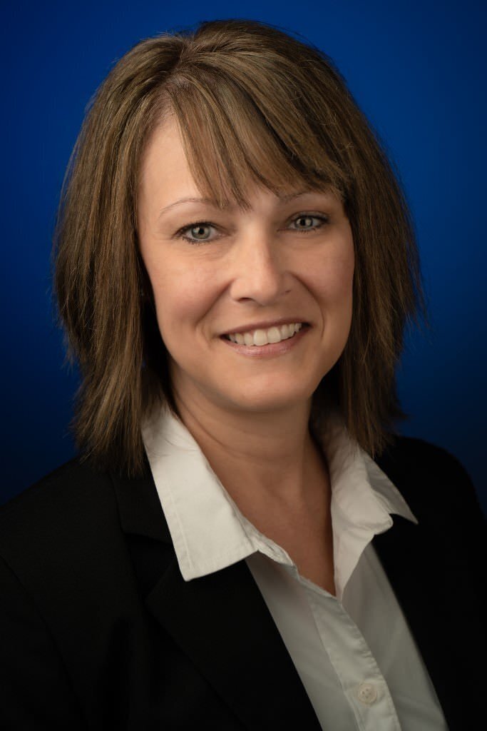 Woman-in-a-white-blouse-and-black-blazer-smiling-against-a-blue-background