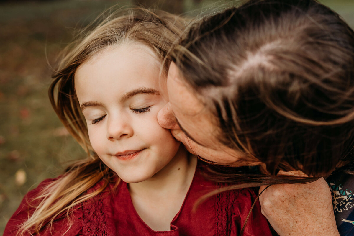 emotive mom kissing daughters cheek in the wind outside
