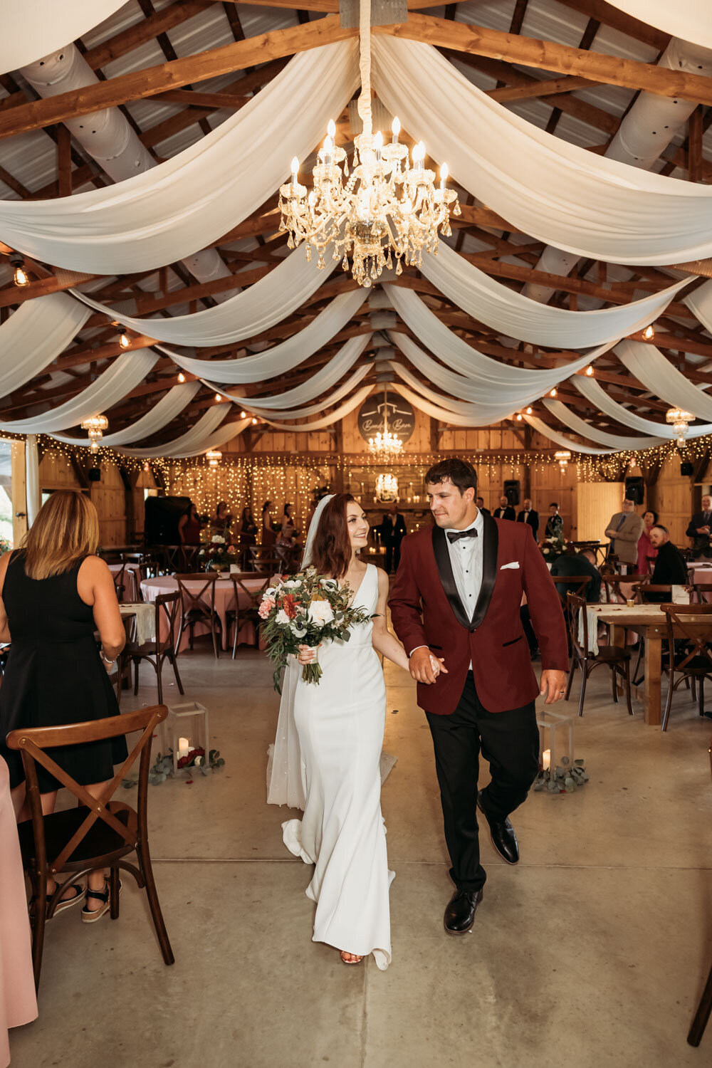 Bride and groom entering reception with smiles and holding hands