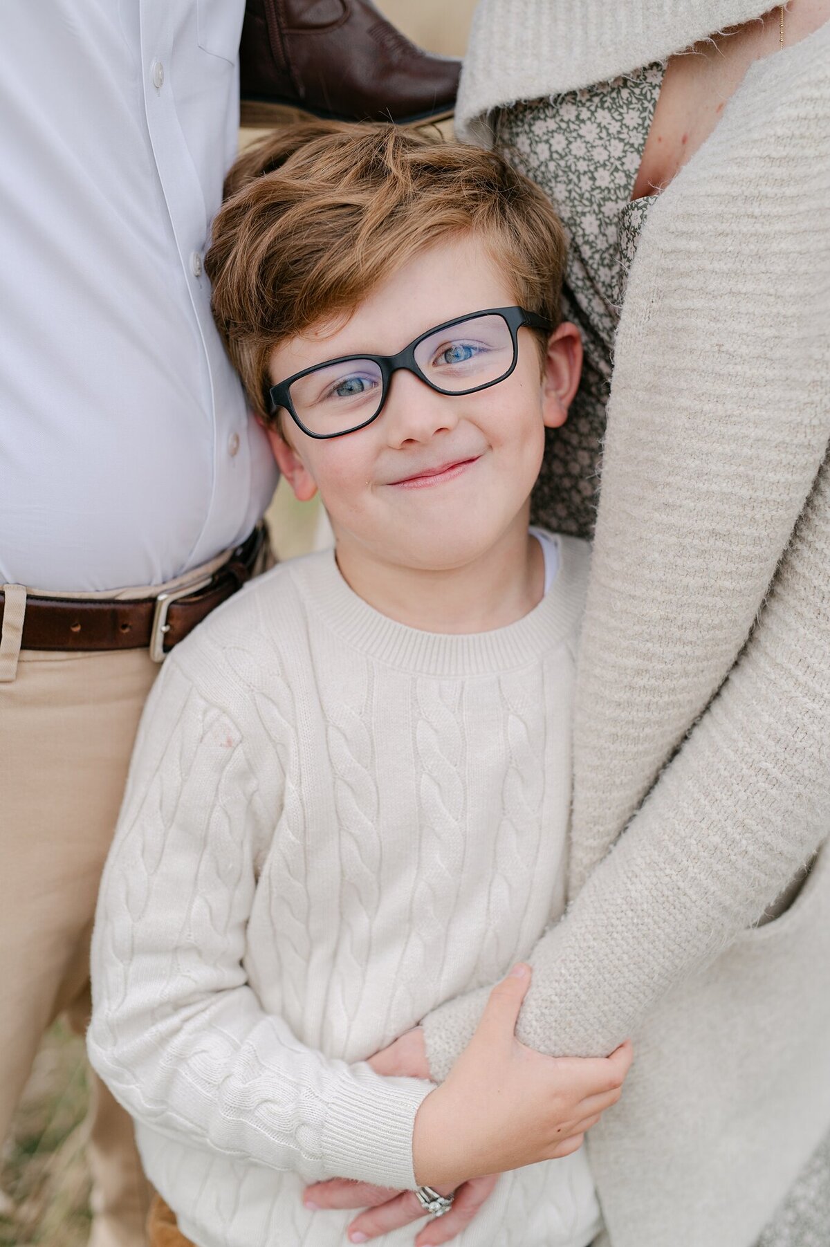 Little boy smiles at the camera while holding his mom's arm in Milwaukee, Wisconsin