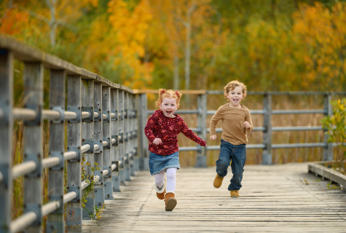 Brother and sister running on a bridge for their fall family photographer session in Burlington, ON