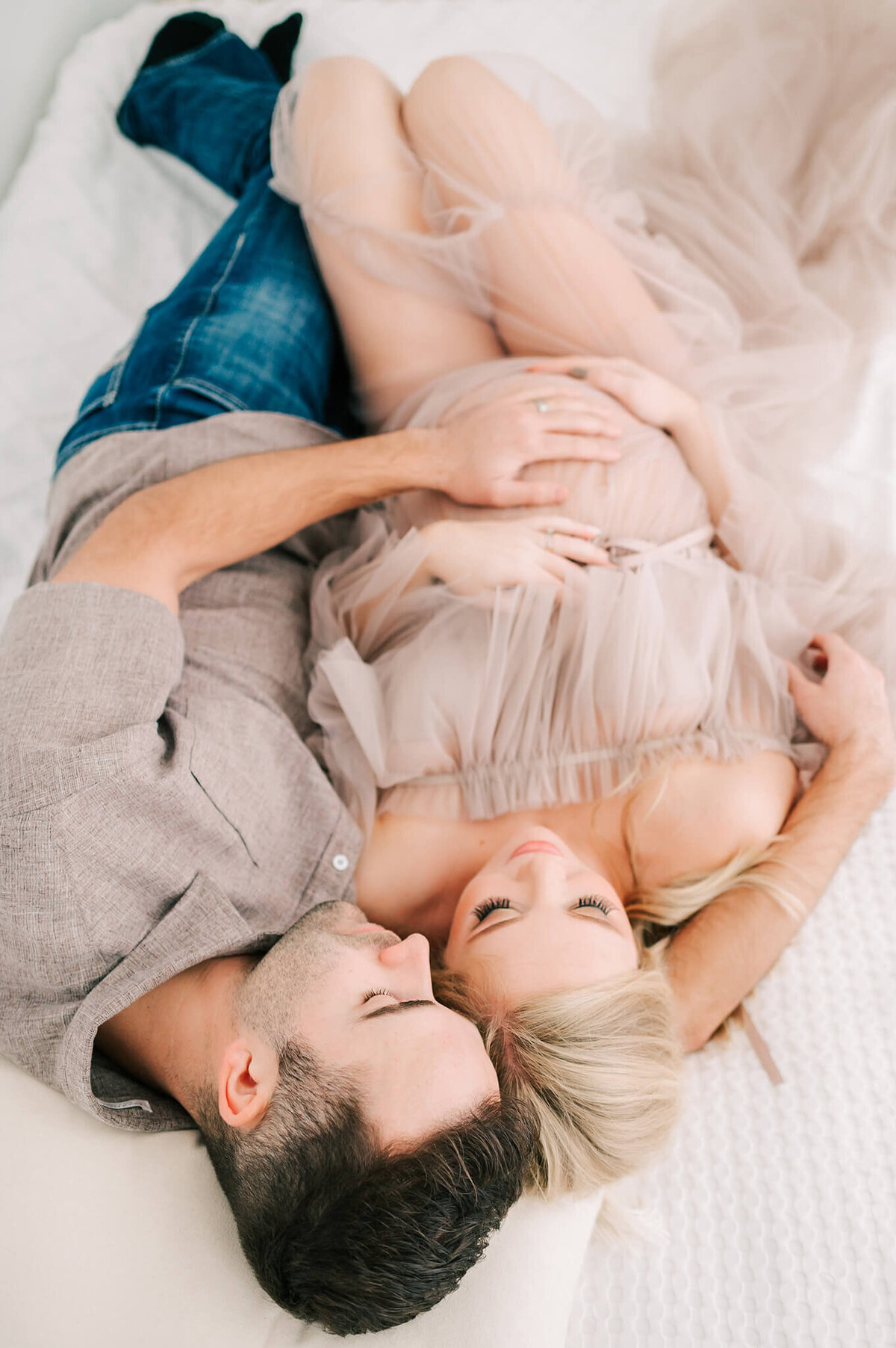 pregnant couple cuddling in bed holding baby bump enjoying Springfield MO maternity photography session