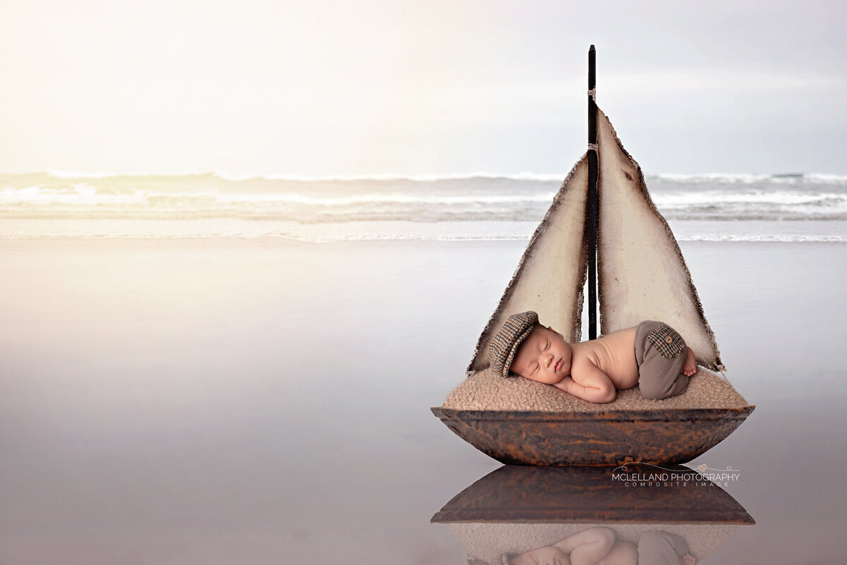 Newborn baby in a small sailboat prop floating on water-themed setup