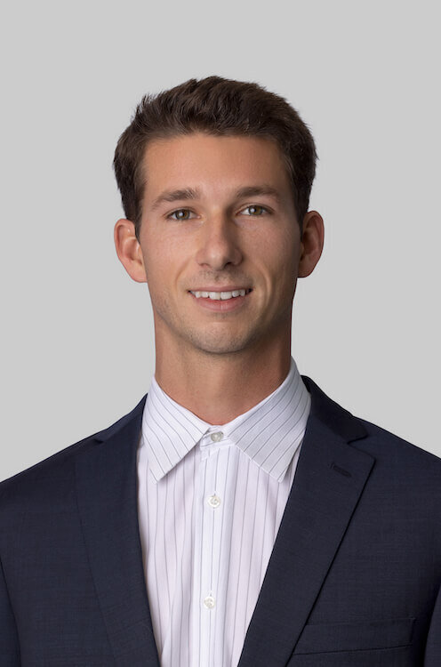 Executive Suite Headshot of a young man wearing a suit without a tie on a white background smiling at the camera