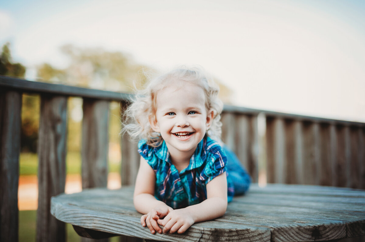 Young girl smiling while laying on a wooden deck during an outdoor child portrait session in Winter Garden, Florida.