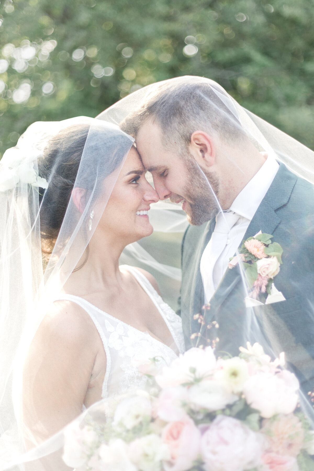 A bride and groom cuddle under the bride's veil