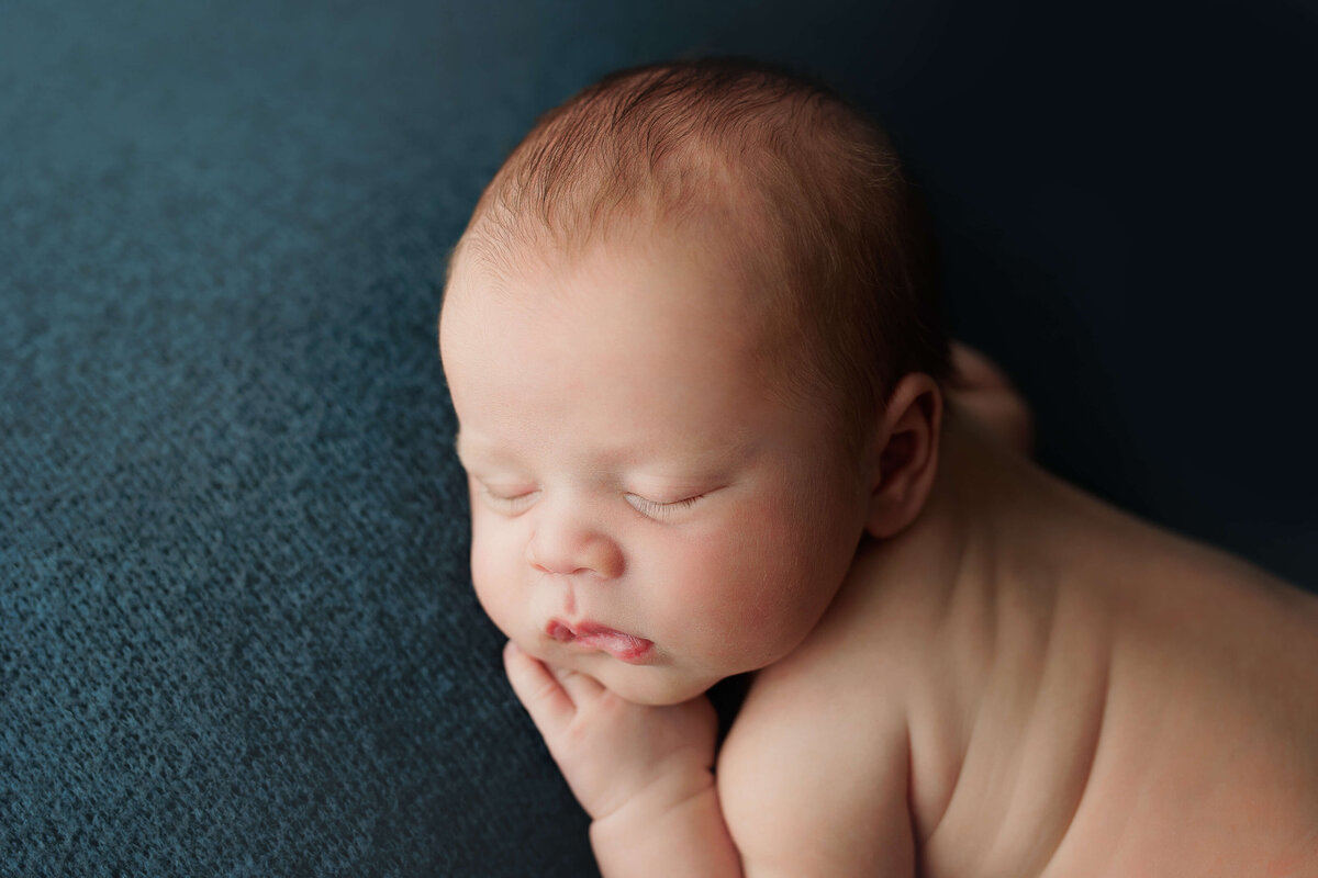 newborn boy laying on his side on a blue backdrop at a photo session