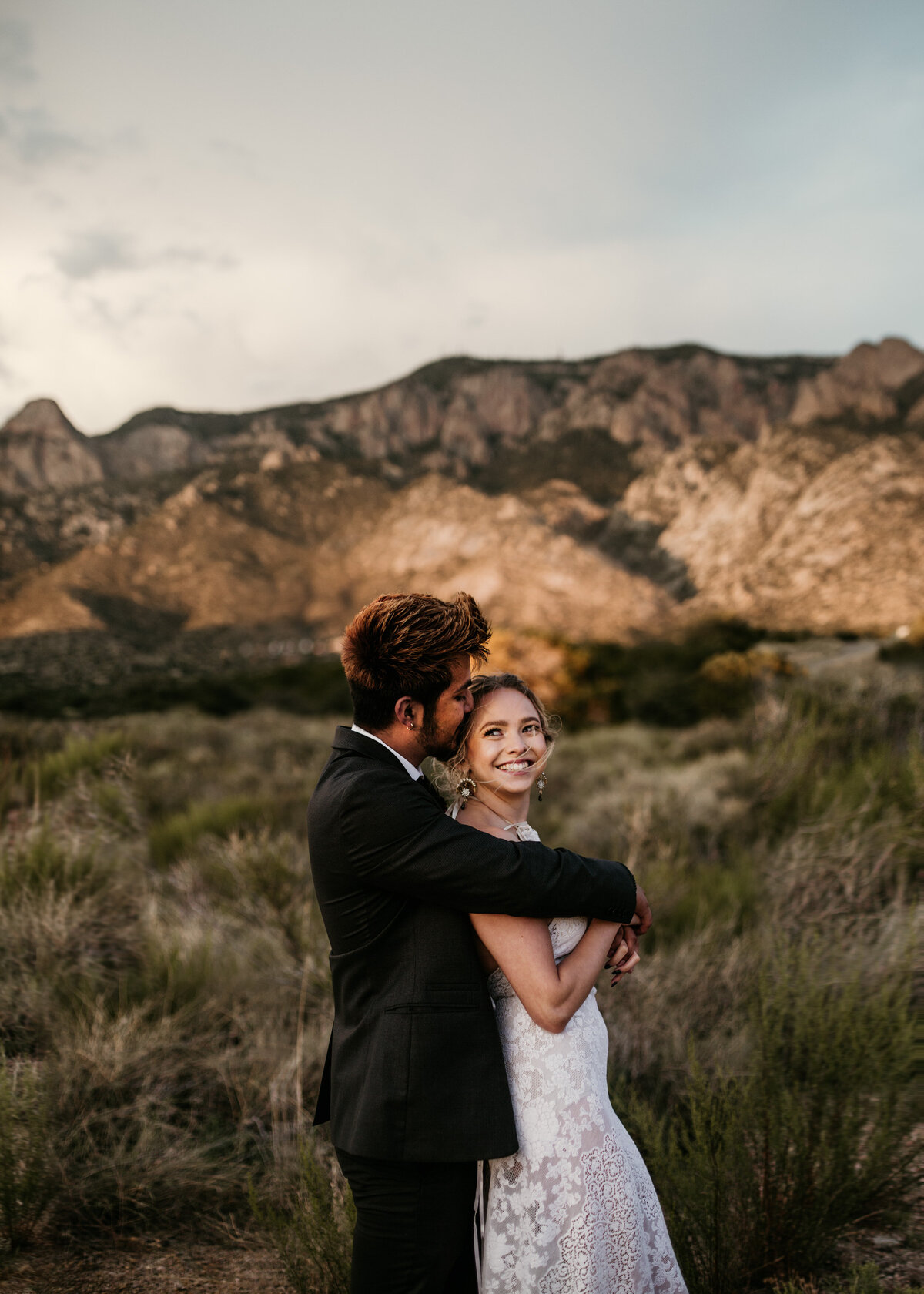 groom kissing bride in desert while she smiles