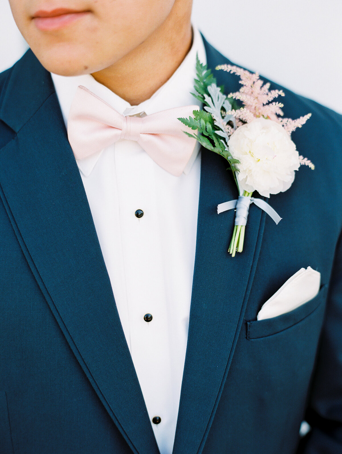 Close-up of groom's white, pink and green boutonniere and pink bowtie