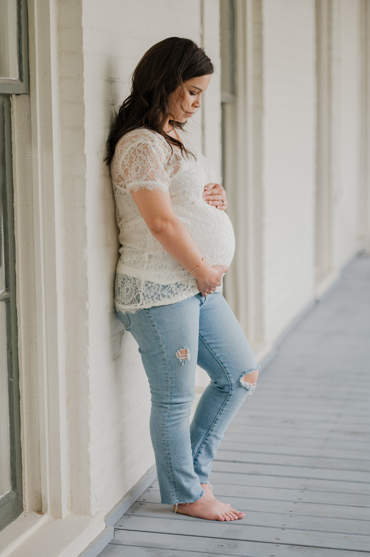 San Antonio maternity photography of a woman in jeans and a lace shirt leaning against a building.