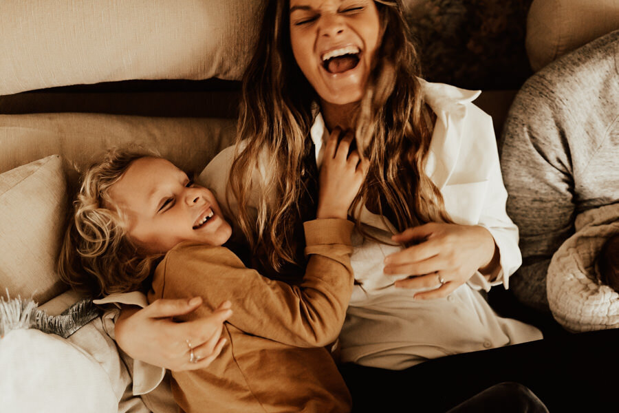 mamma och son sitter i soffa och skrattar under familjefotografering