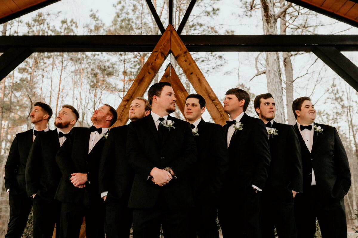 groomsmen standing together in a line outside of the wedding venue looking off into the distance