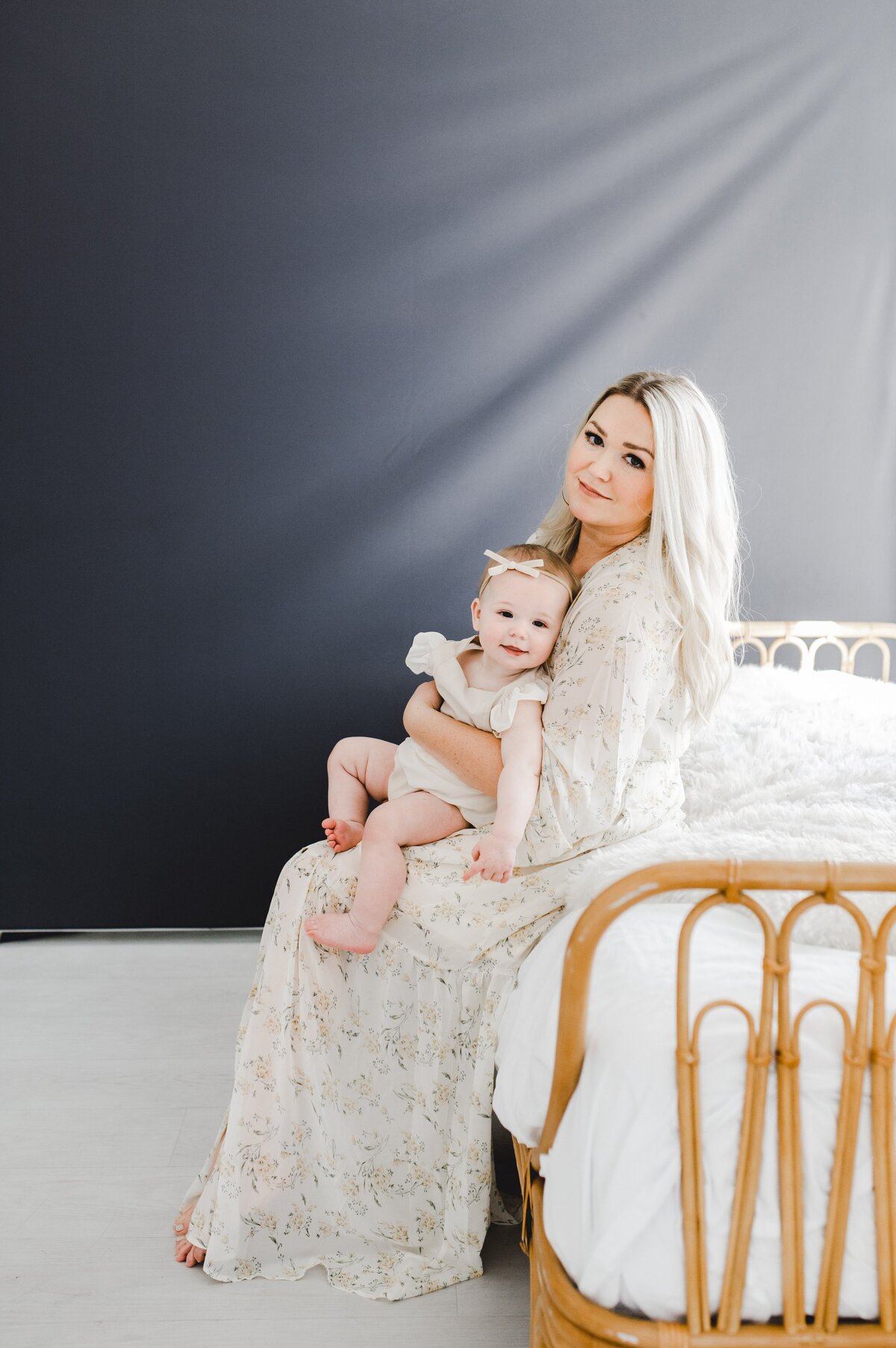 Mommy and baby girl sitting on a bed in a studio.