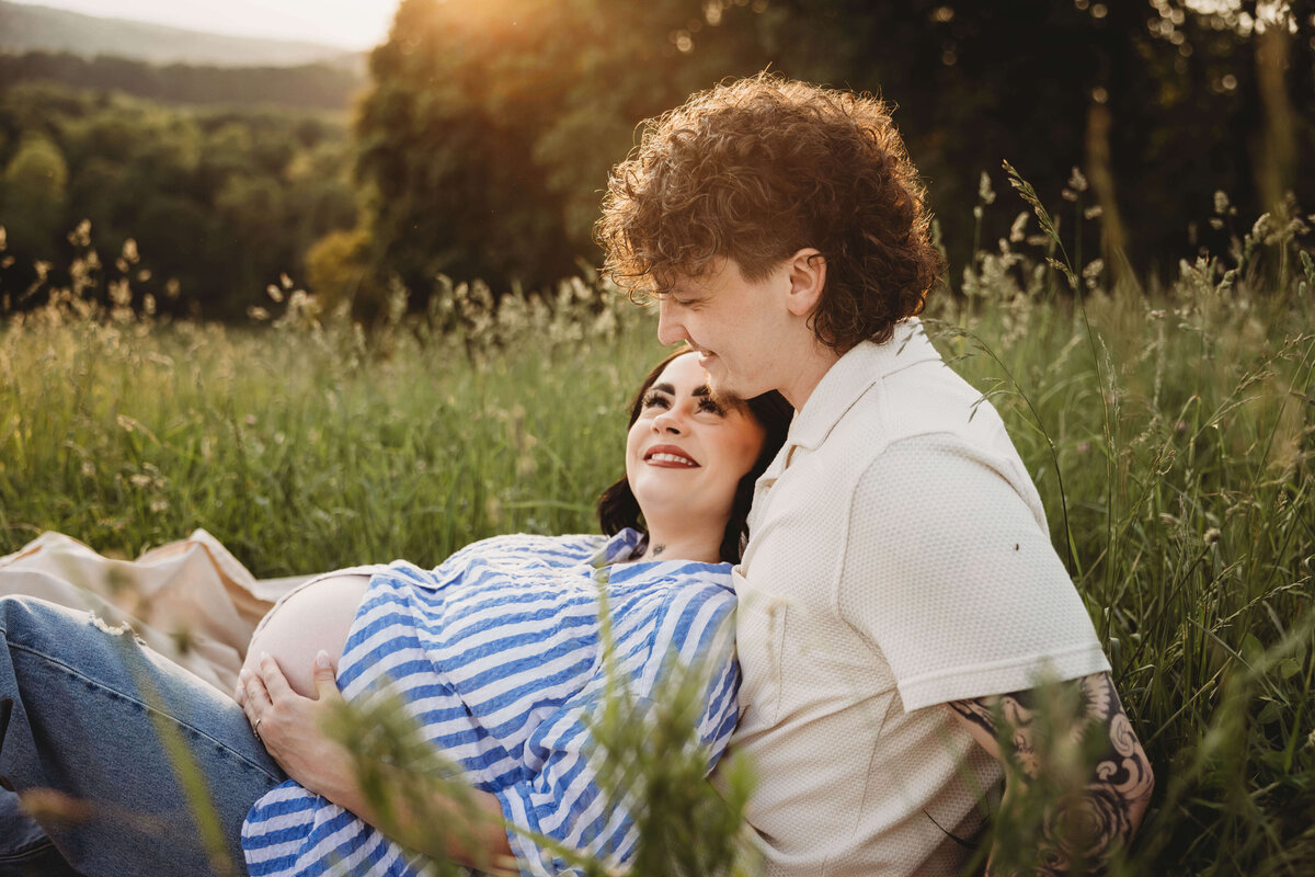 mom and dad cuddling on blanket in tall grass in portrait session with reva davis photography