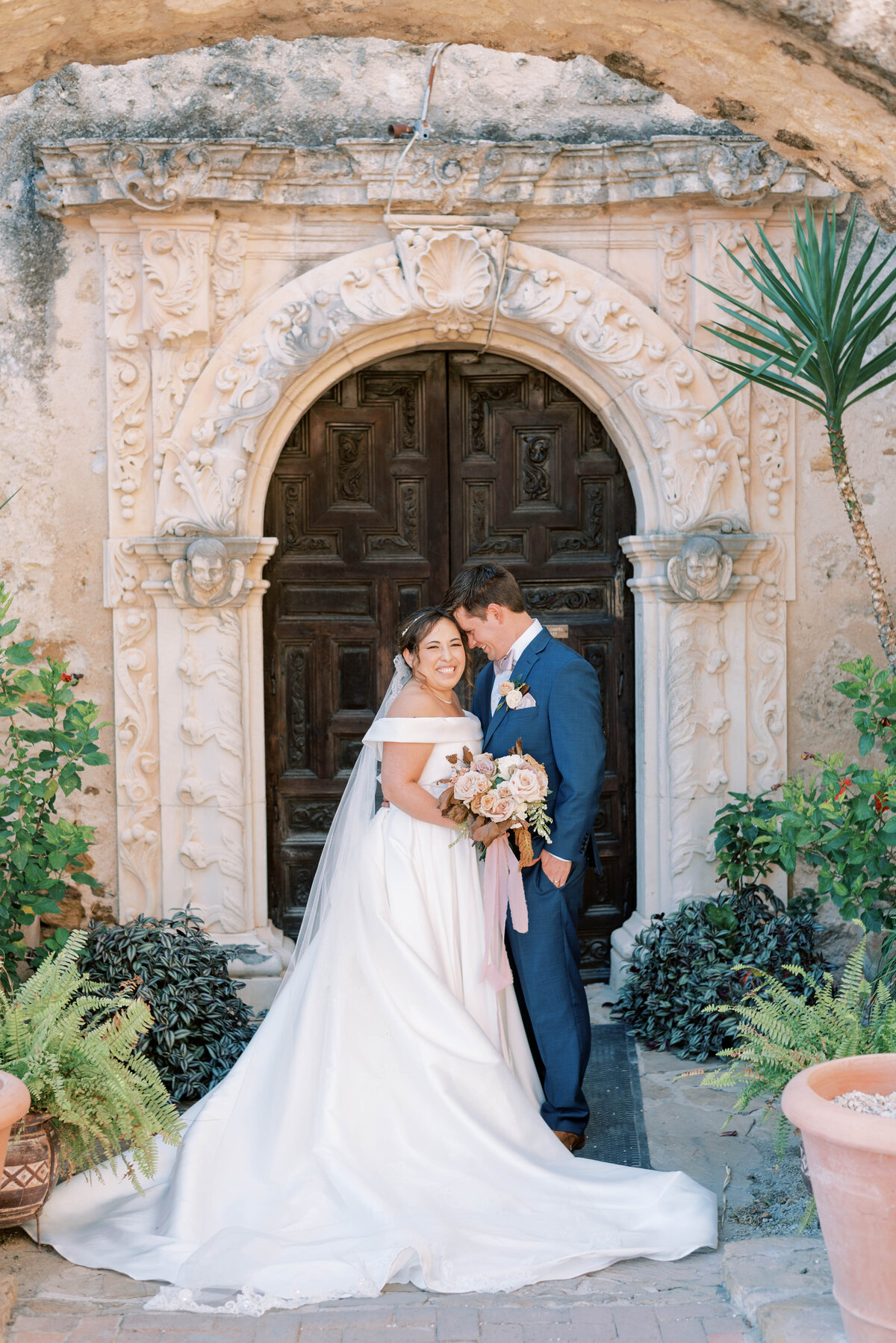 Bride and groom posing in front of a large wooden arched door