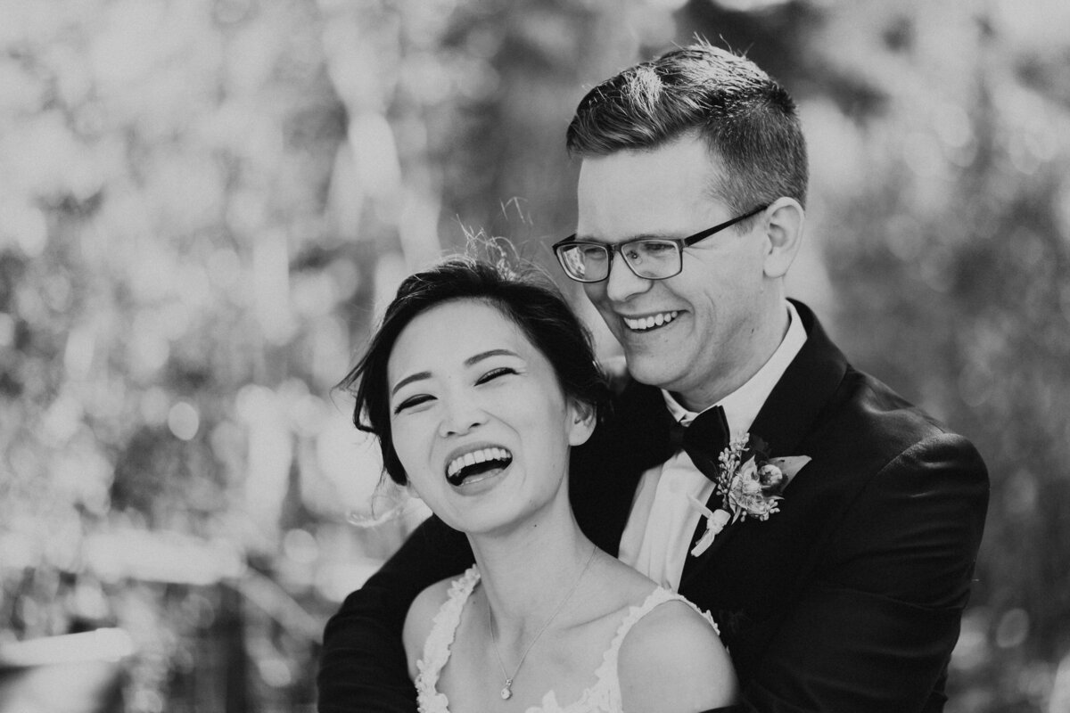 Wedding photography, black and white image of bride and groom smiling together with his arms around her