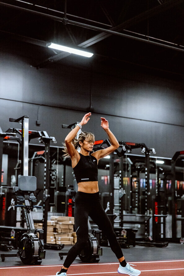 Girl does jumping jacks on the track in an all-black gym.