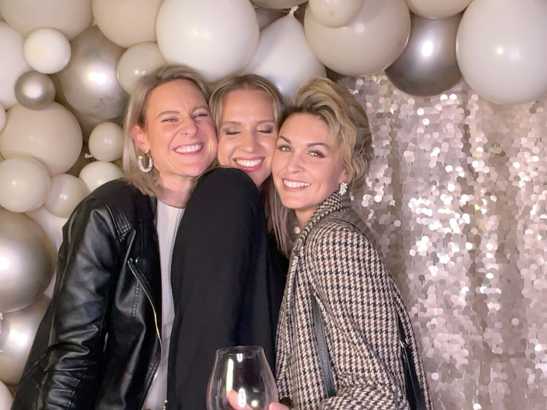 three women wearing neutral colours in front of a gold sequin and balloon backdrop in a photo booth capture in christchurch