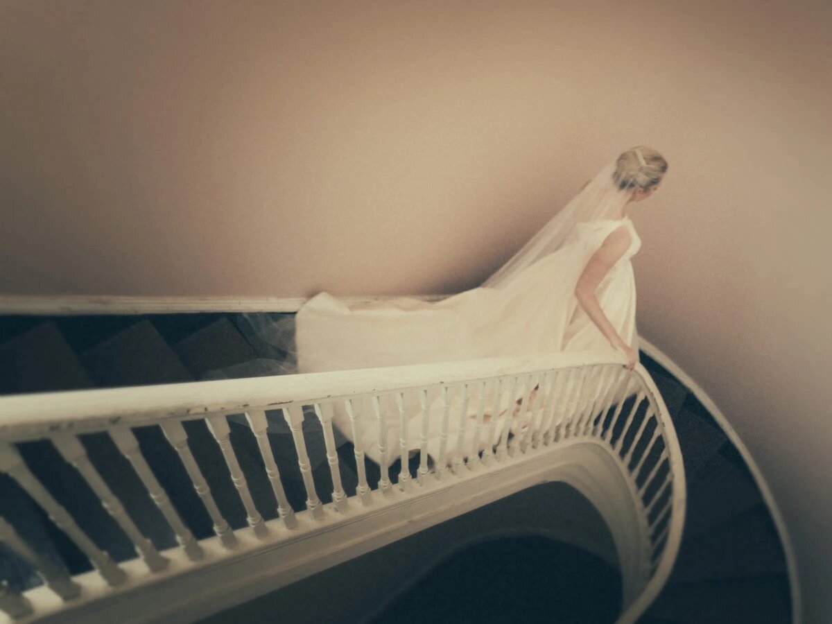 A bride reclines on a curved staircase, her wedding dress cascading down the steps