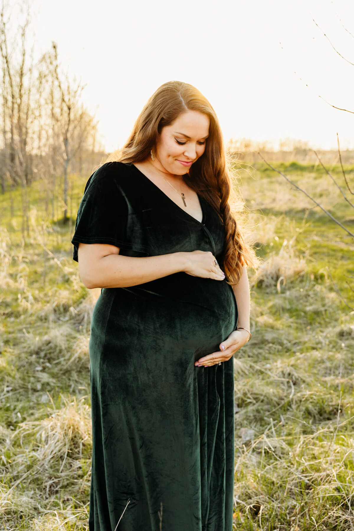 stunning mother to be holding and admiring her baby bump with a gorgeous sunset behind her