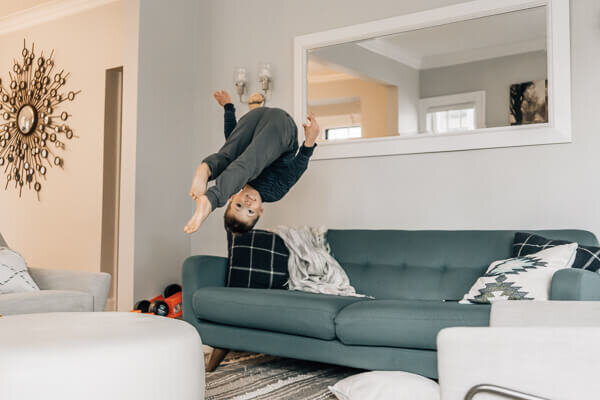A little boy caught in midair doing a flip onto his couch during a family photography session by Kate Simpson.