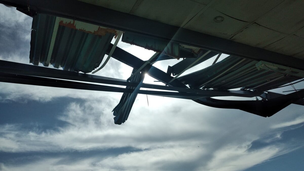 Exposed ceiling beams and missing roof panels revealing the sky above the classroom.