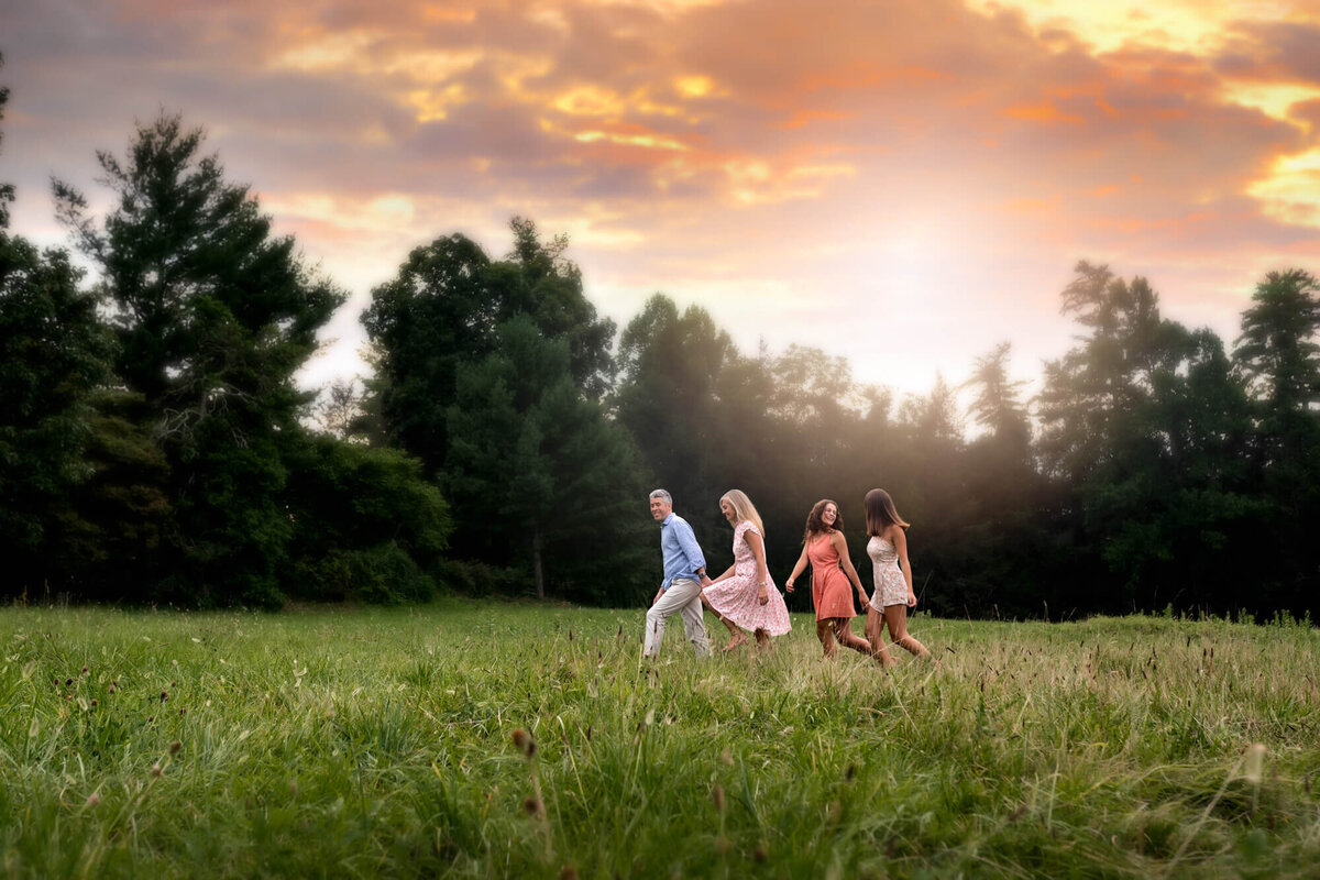 A dad, mom and their two daughters walking through a filed at sunset
