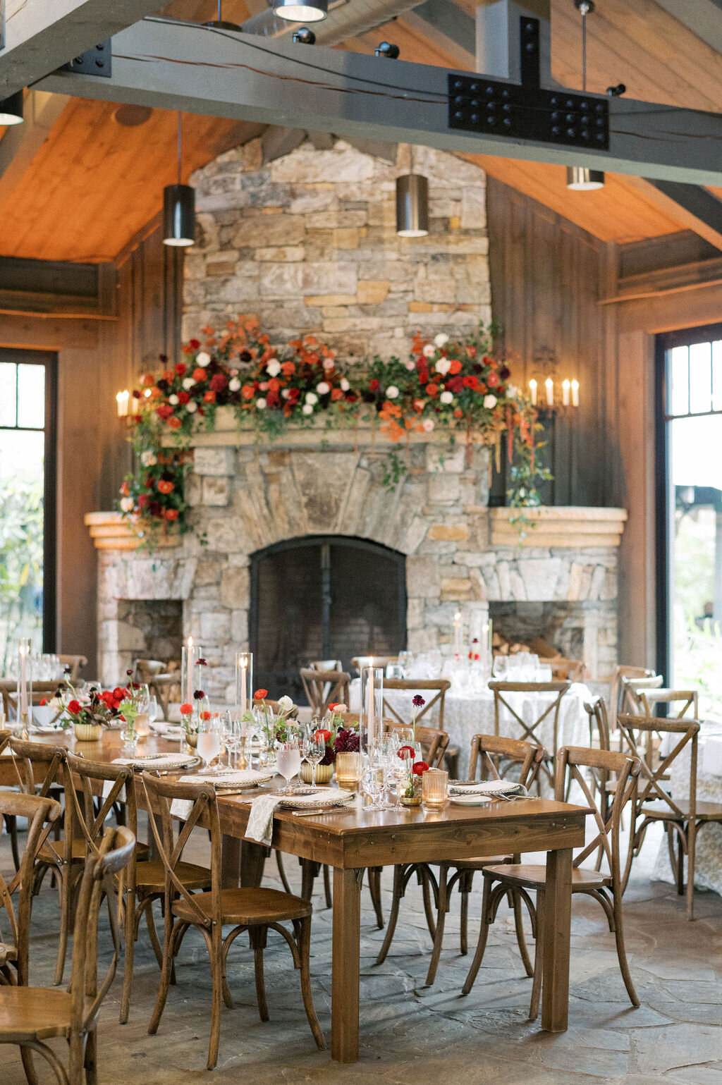 Luxury wedding reception with long tables, bud vases and taper candles, stone fireplace with red floral arrangements at Old Edwards Inn in Highlands, NC. 