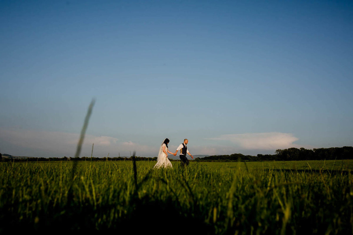 a wedding couple walking through a field during the wedding photography portrait session