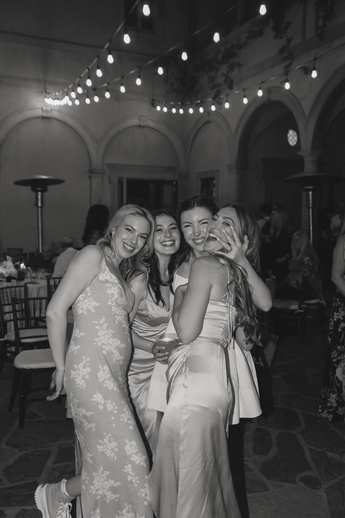 bride with her bridesmaids close group picture all laughing during reception drinks in hand photo is in black and white