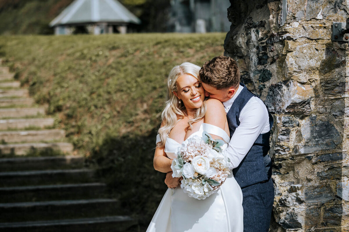 A bride and groom embracing in front of a stone wall
