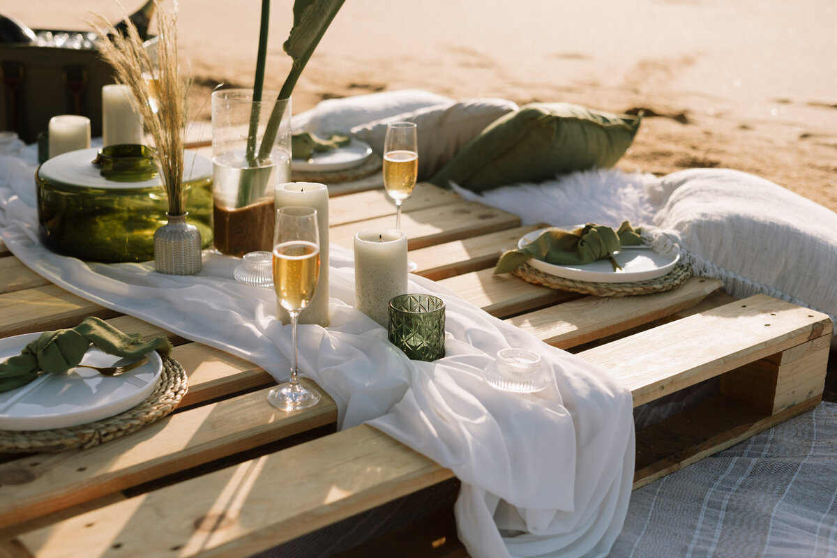 A beach picnic has been set up with champagne glasses , its a sunrise photo that catches golden sunrise light